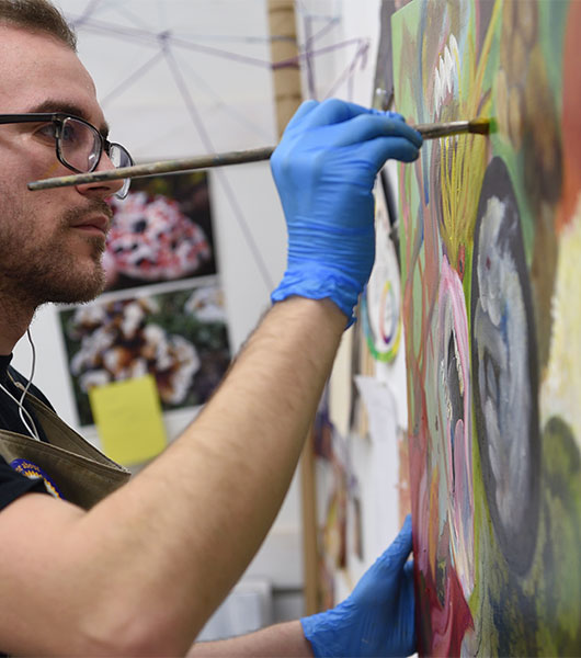 Painting student uses a brush to add detail to a colorful artwork.