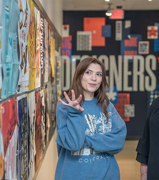 Graphic design student discusses work displayed on a studio wall.